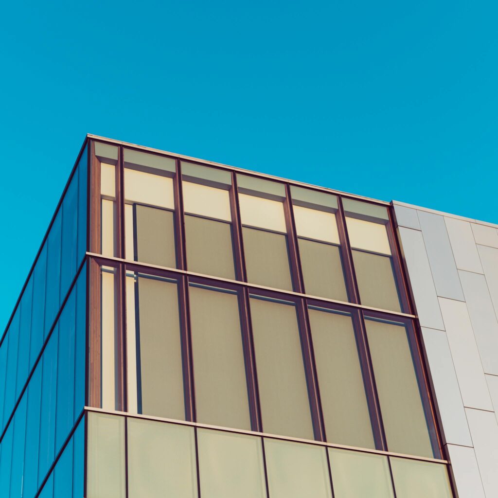 A contemporary glass and metal building facade under a bright blue sky, showcasing modern architecture.