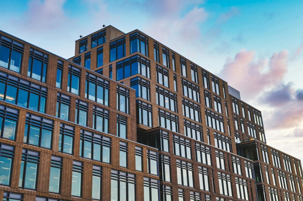 Contemporary multistory building with wooden facade and glass windows under a cloudy blue sky.